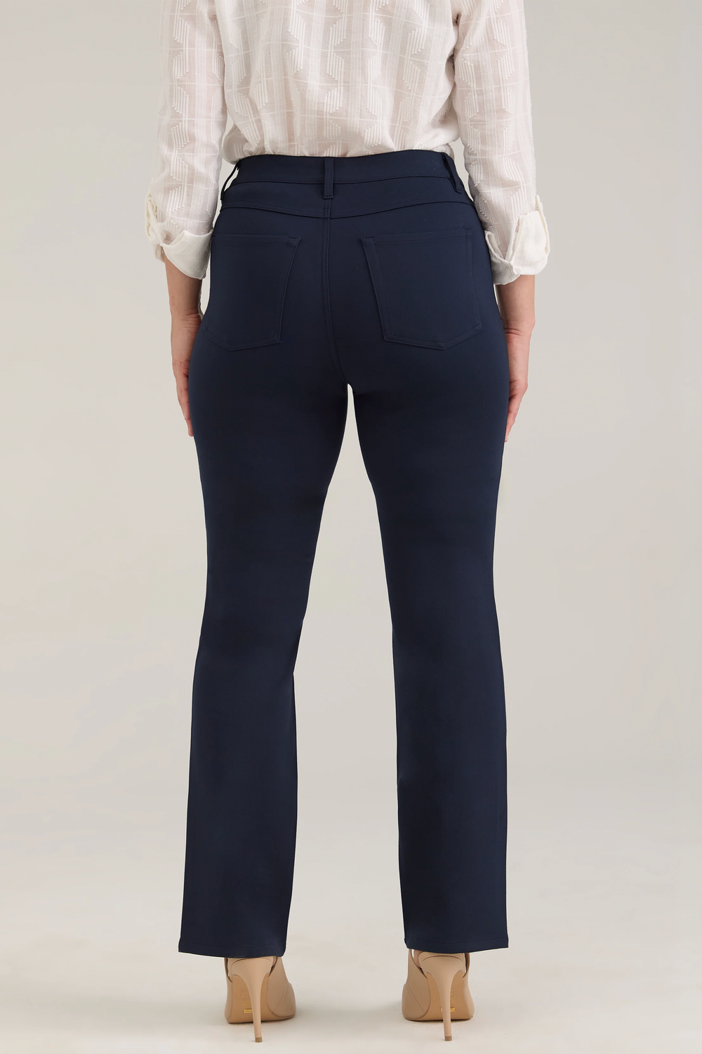 A woman modelling a white blouse and navy pants standing in front of a light beige background. 
