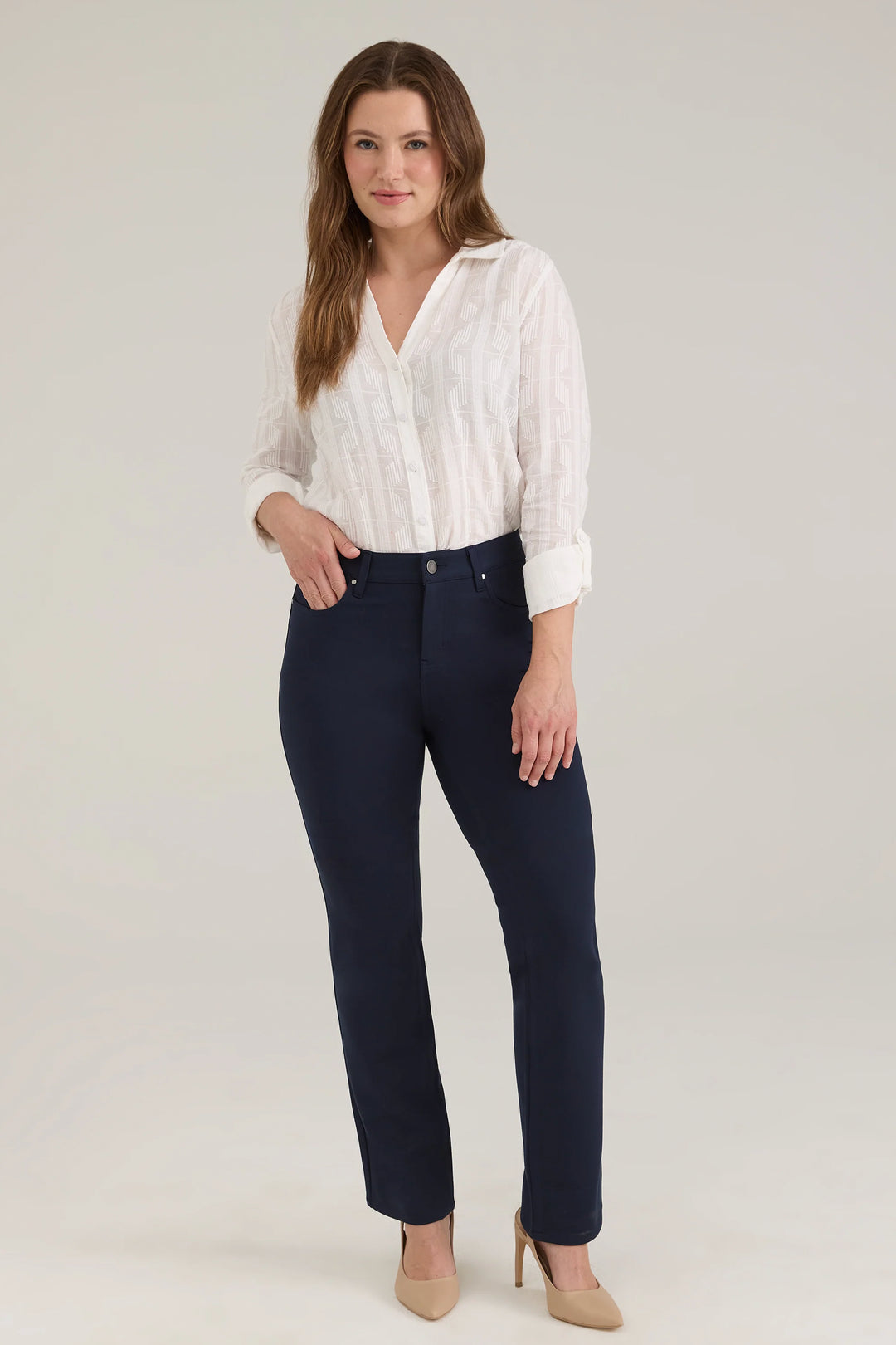 A woman modelling a white blouse and navy pants standing in front of a light beige background. 
