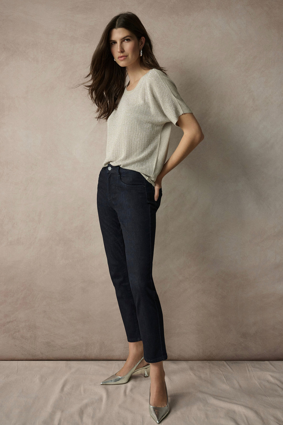 Woman wearing a light-colored top and dark jeans against a plain background