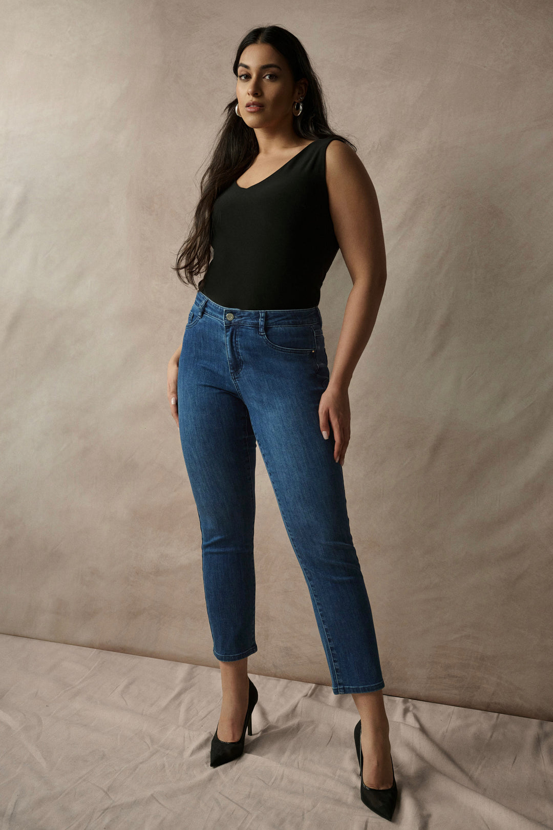 Woman wearing a black top and blue jeans against a beige background