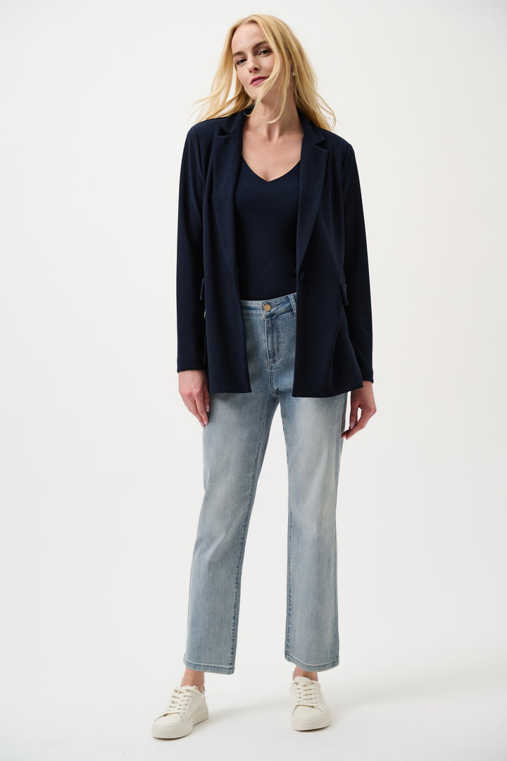 Woman wearing a black blazer, black top, light blue jeans, and white sneakers on a white background