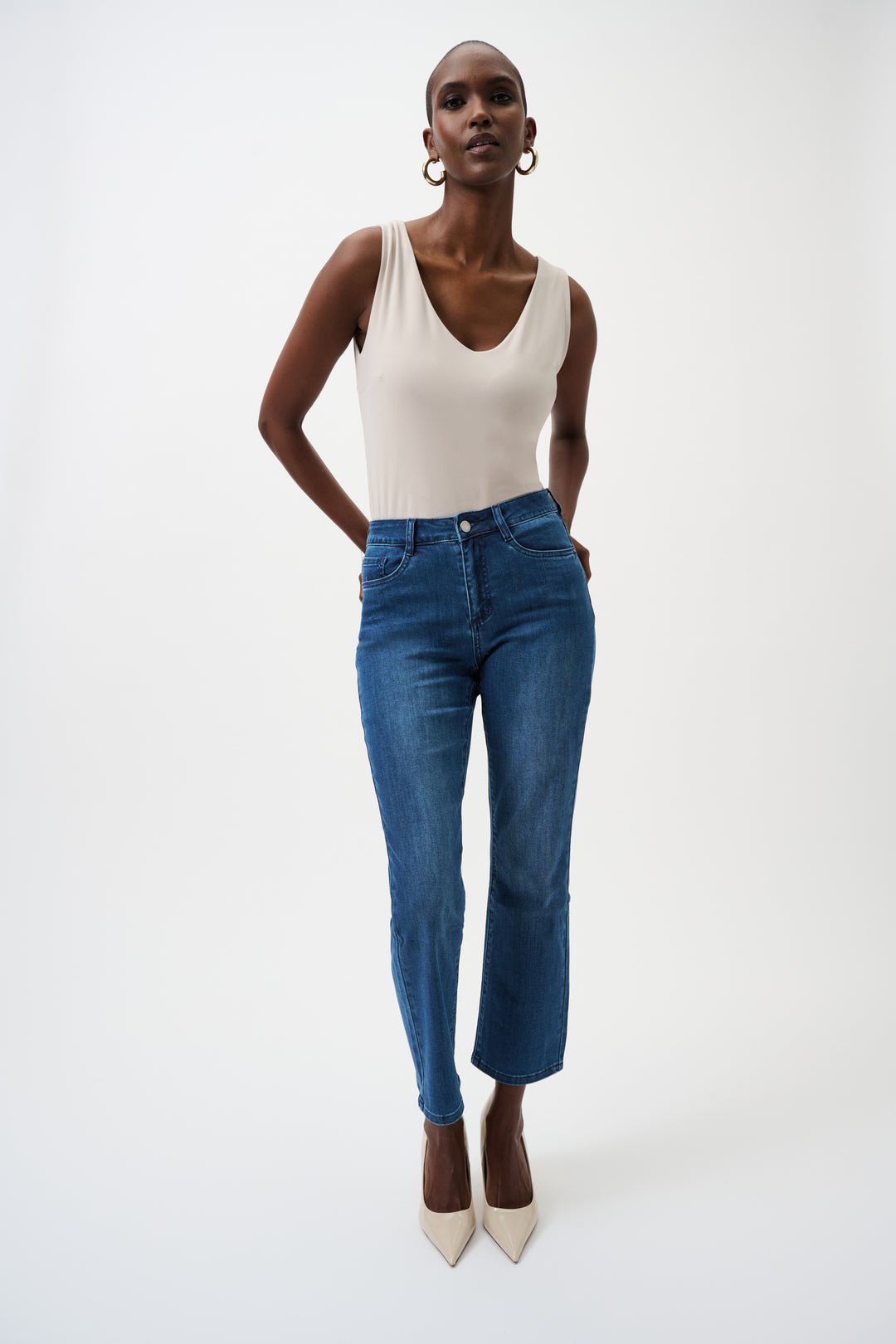 Woman wearing a beige tank top and blue jeans on a white background