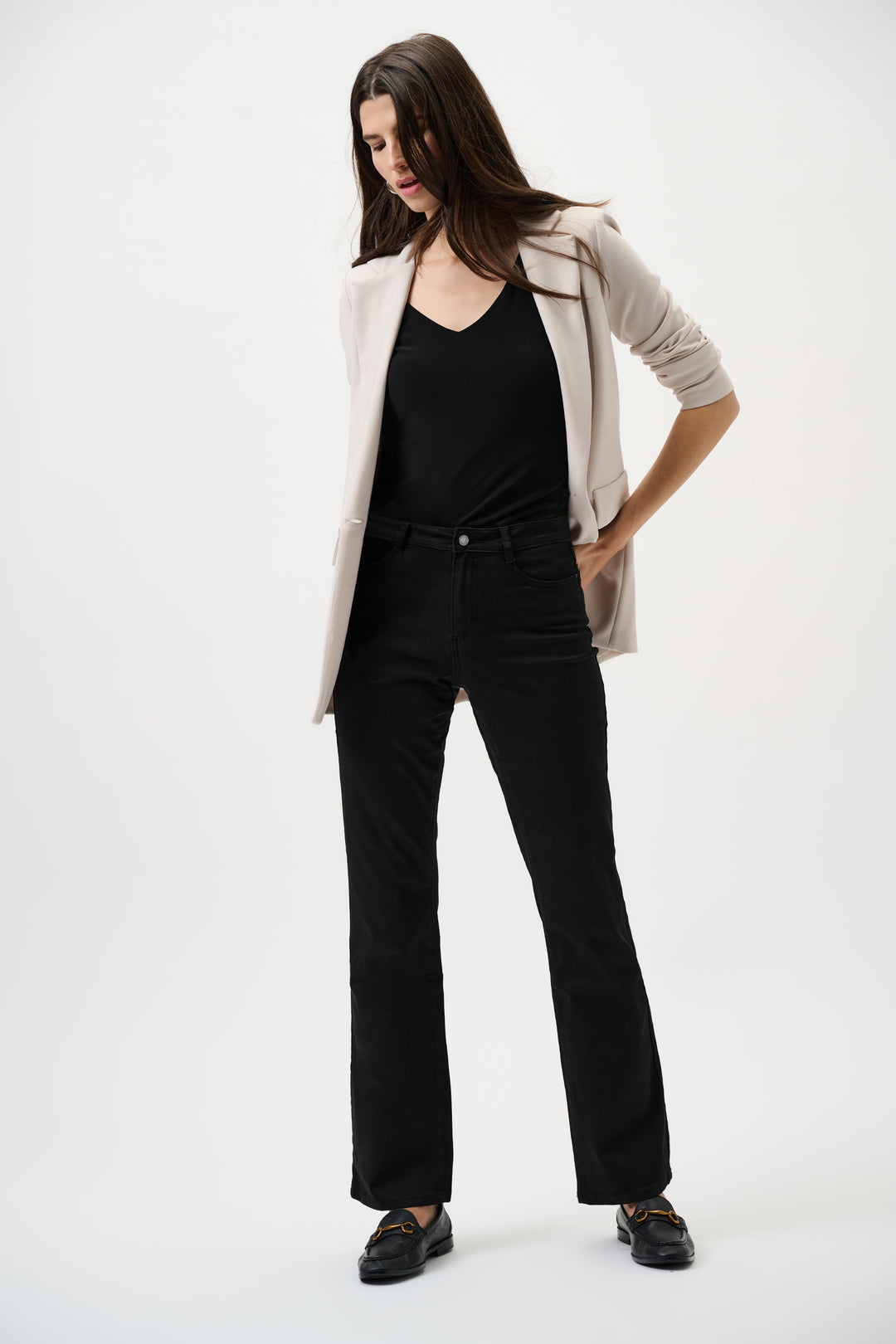 Woman wearing a beige blazer, black top, and black jeans on a white background