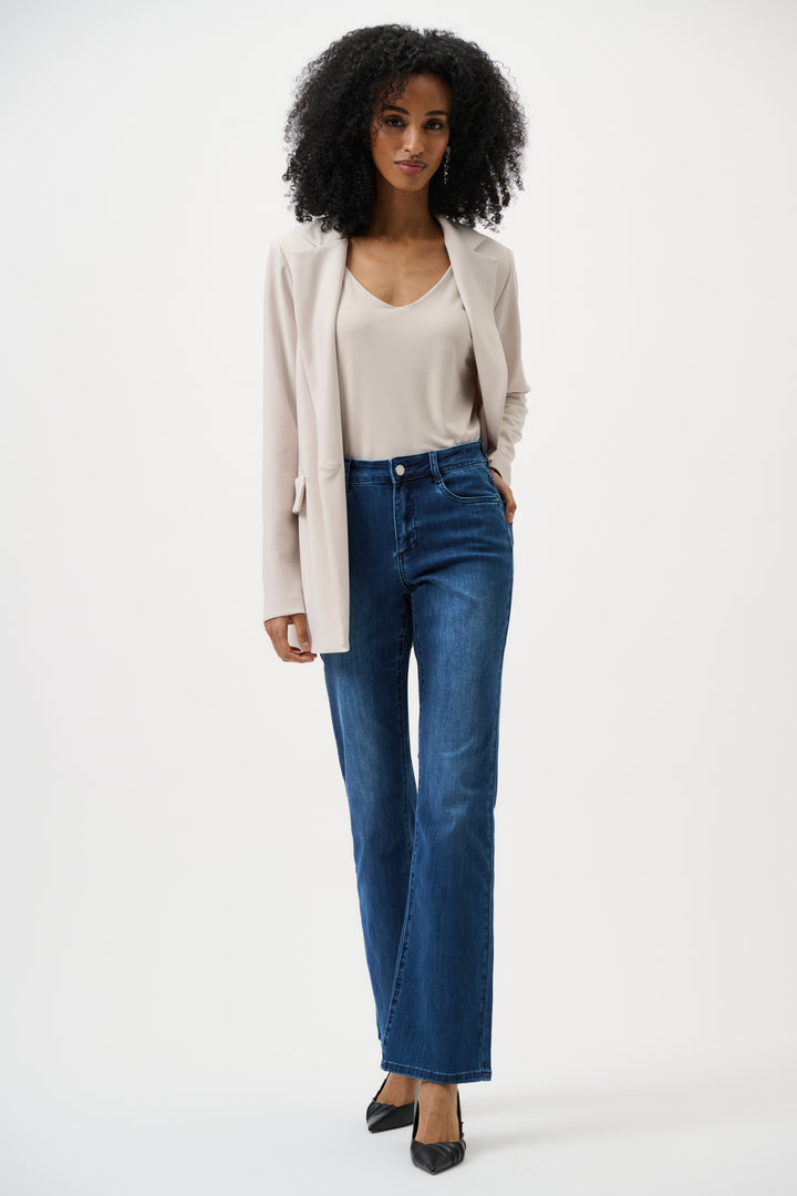 Woman wearing a beige blazer, white top, and blue jeans on a white background