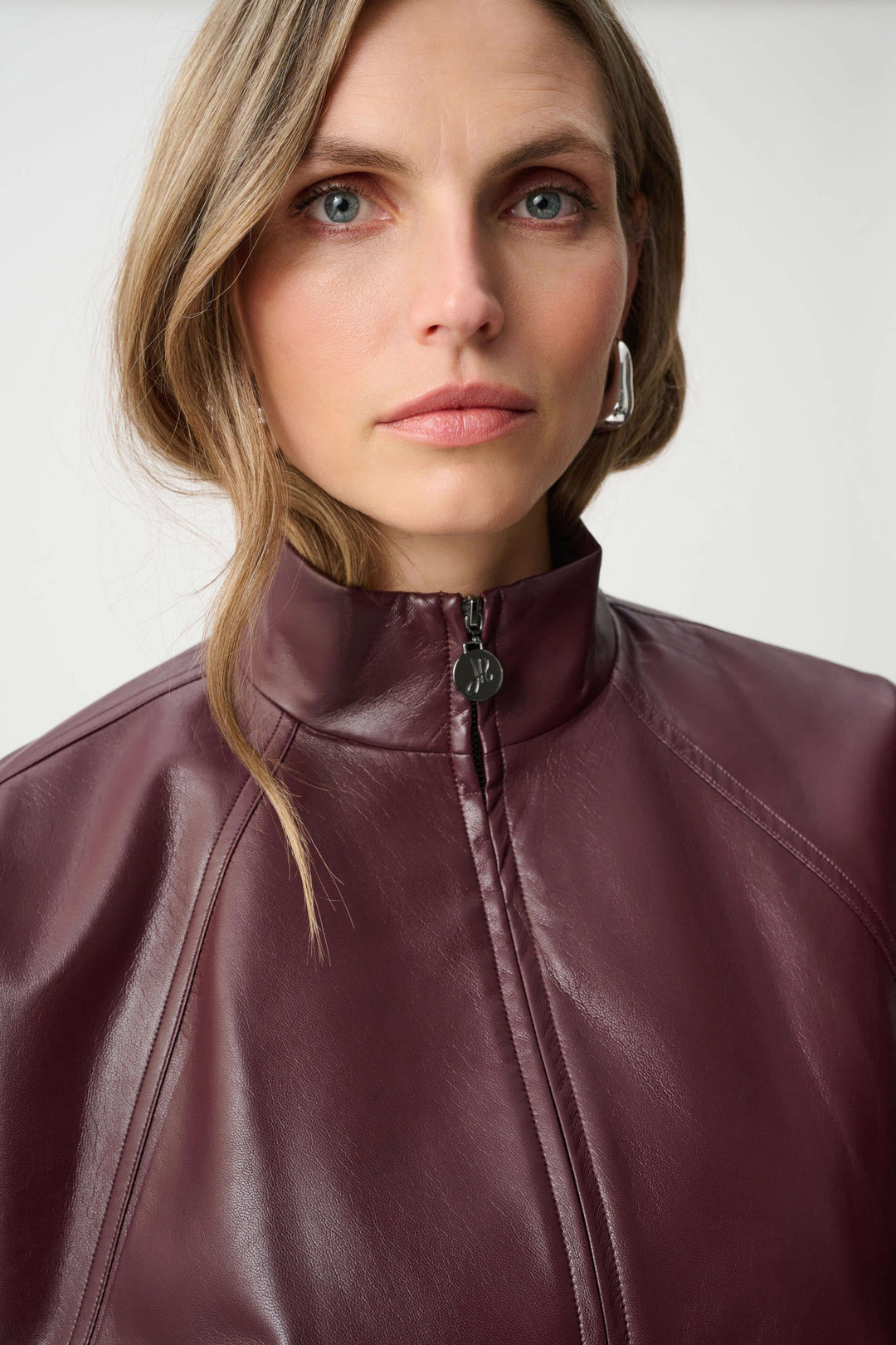 Close-up of a person wearing a maroon pleather bomber jacket with a plain background