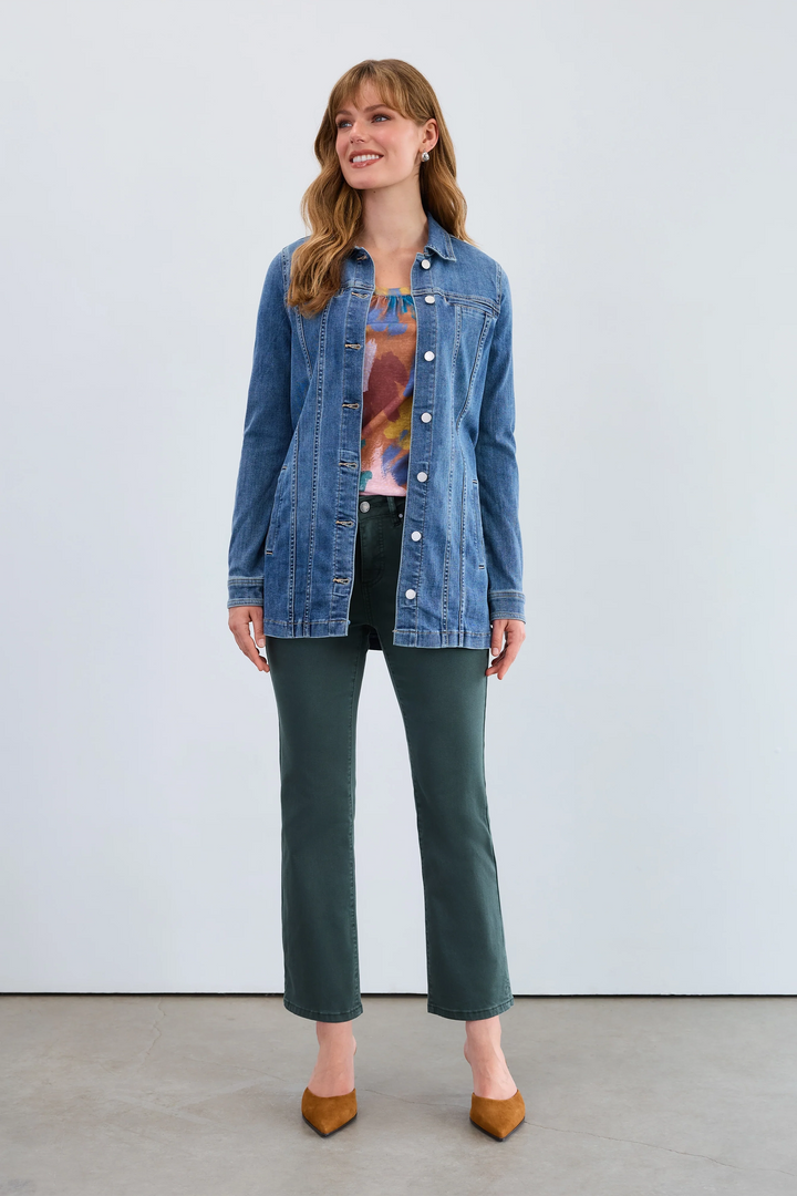 Woman wearing a denim jacket over a graphic t-shirt with green pants against a white background
