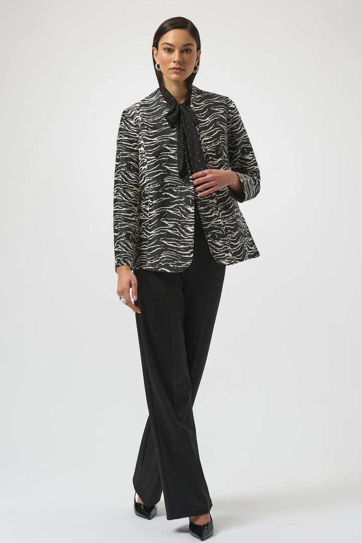 Woman wearing a black and white patterned blazer jacket with black pants on a white background