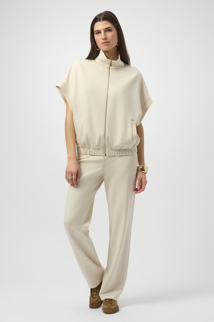 Woman wearing a cream-colored outfit with a cape-like top and pants on a white background