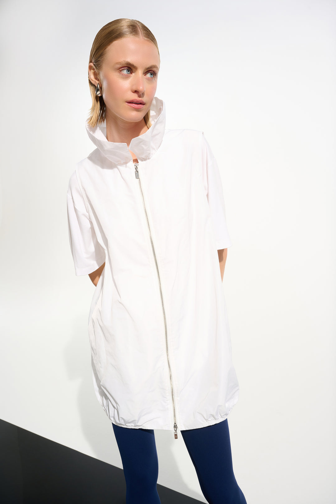 Woman wearing a white light long vest with a front zipper on a plain background