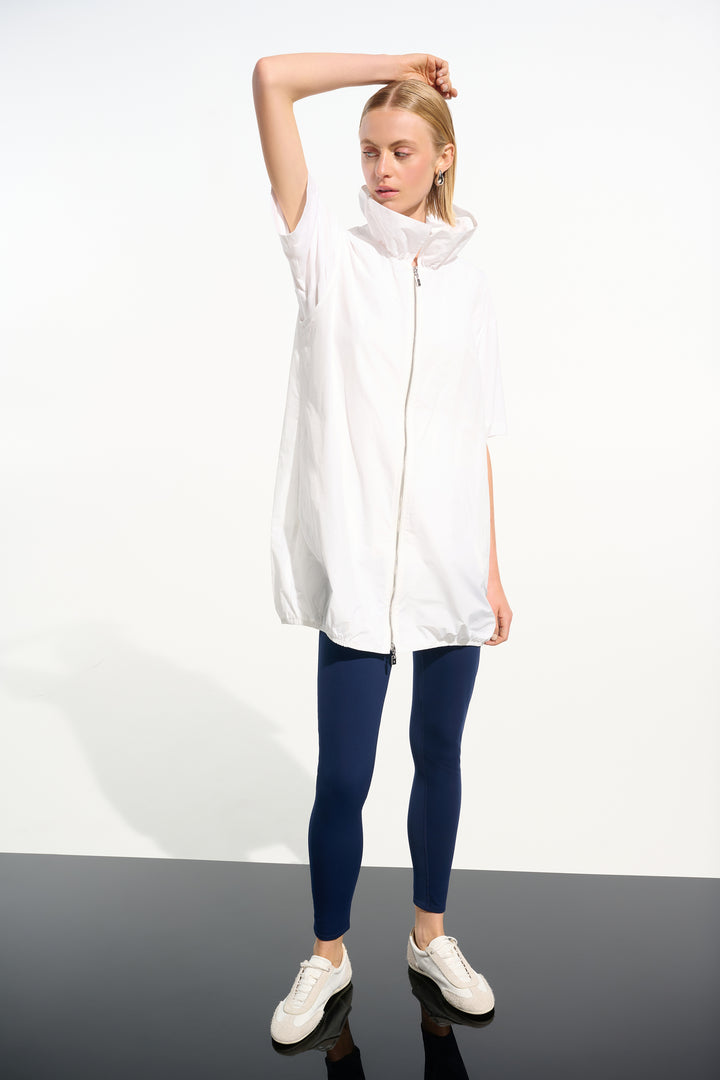 Woman wearing a white light long vest and blue leggings on a white background