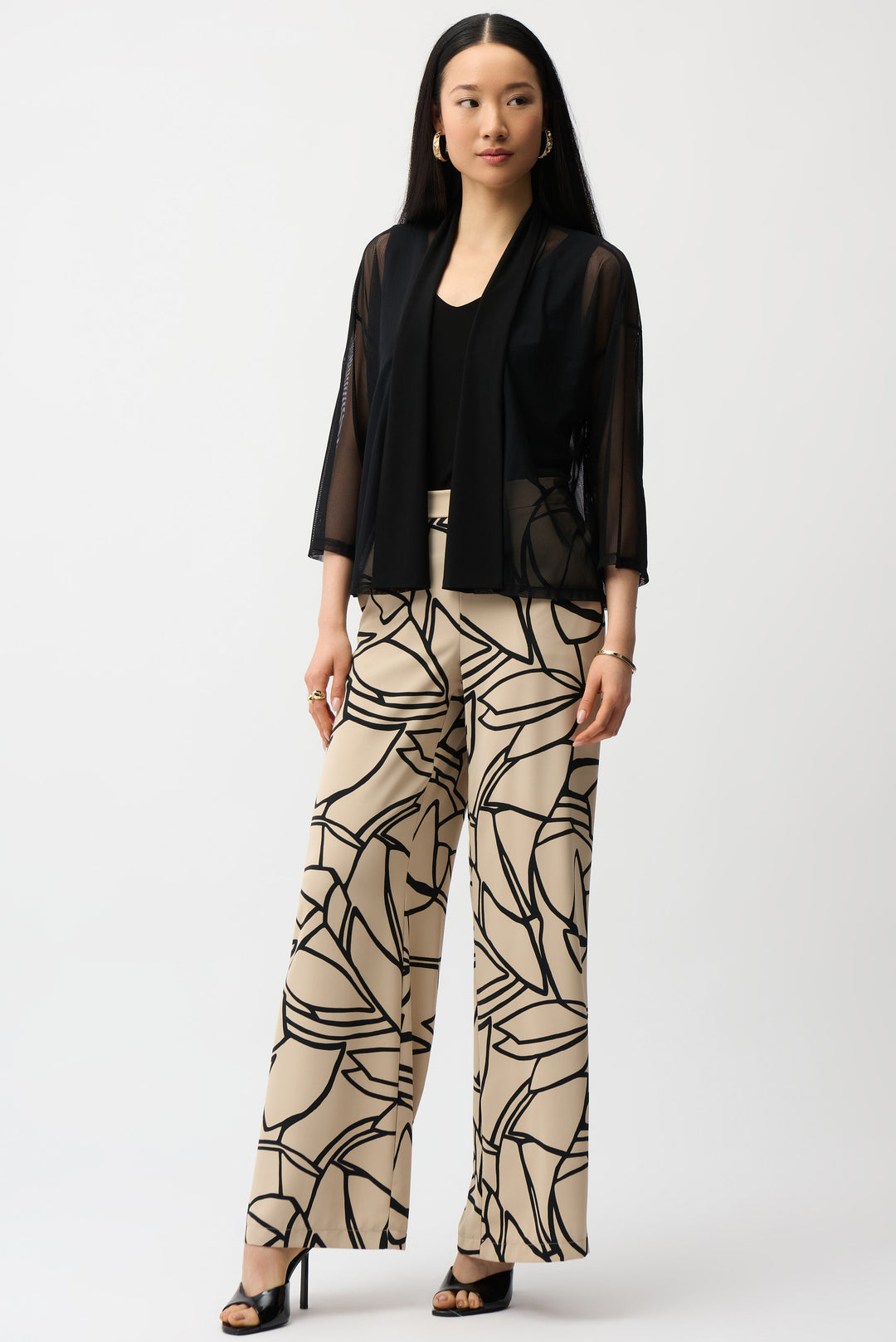 Woman wearing a black mesh open cardigan and beige patterned pants on a white background