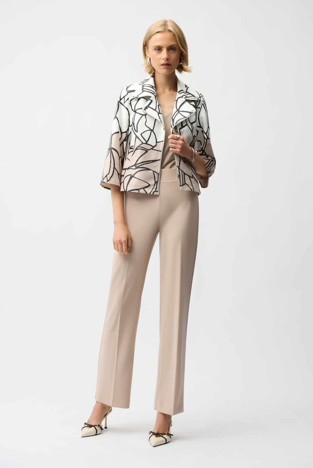 Woman wearing an abstract print zip jacket and beige pants on a white background