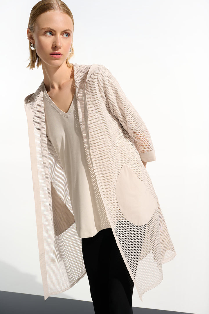 Woman wearing a beige mesh long cardigan over a white blouse with a plain background