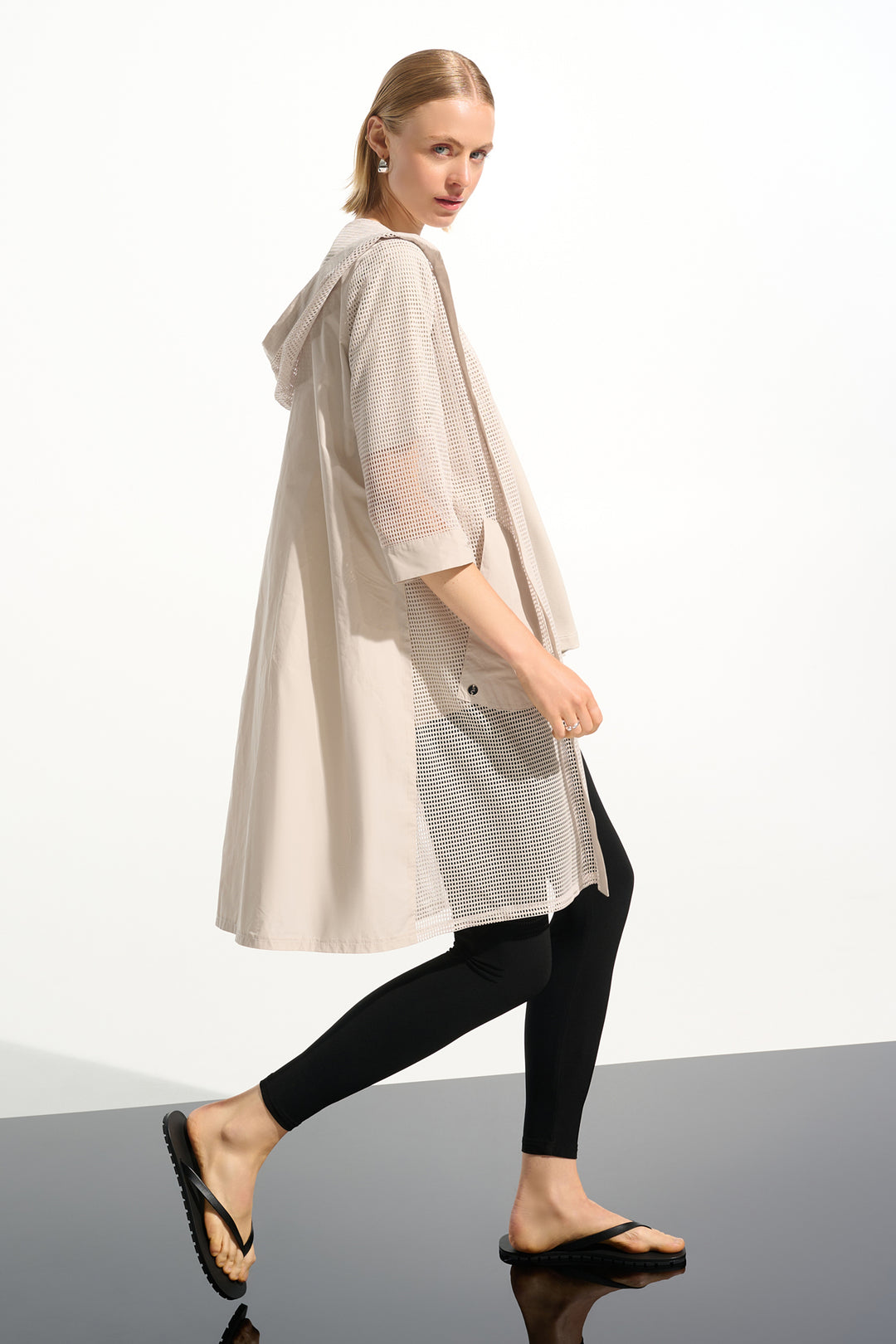 Woman wearing a beige long mesh cardigan and black pants on a white background