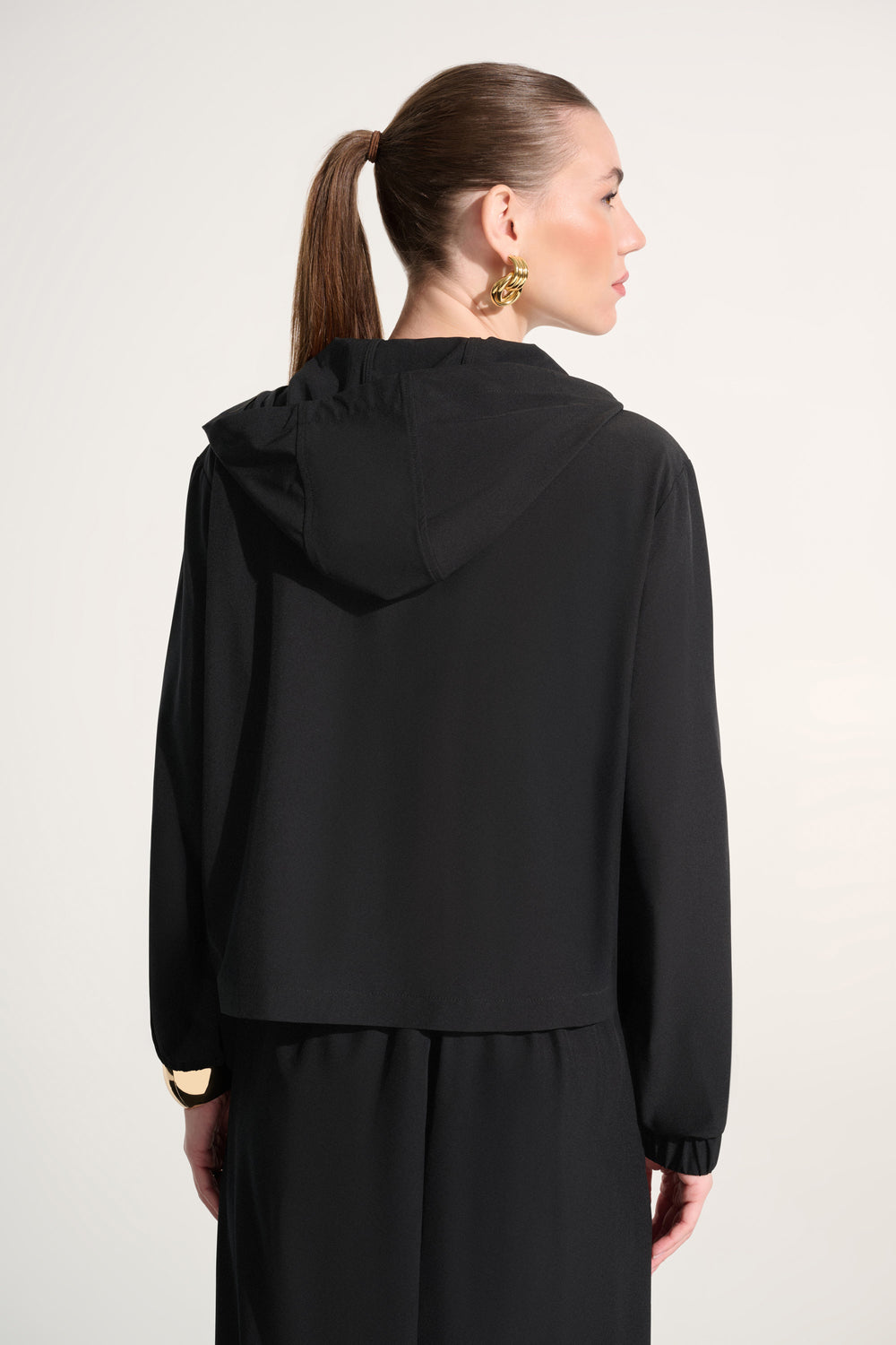 Woman wearing a black outfit with a hood against a white background