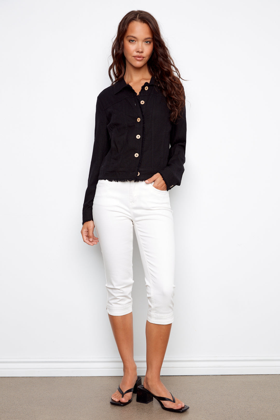 Woman wearing a black jacket and white pants against a white background