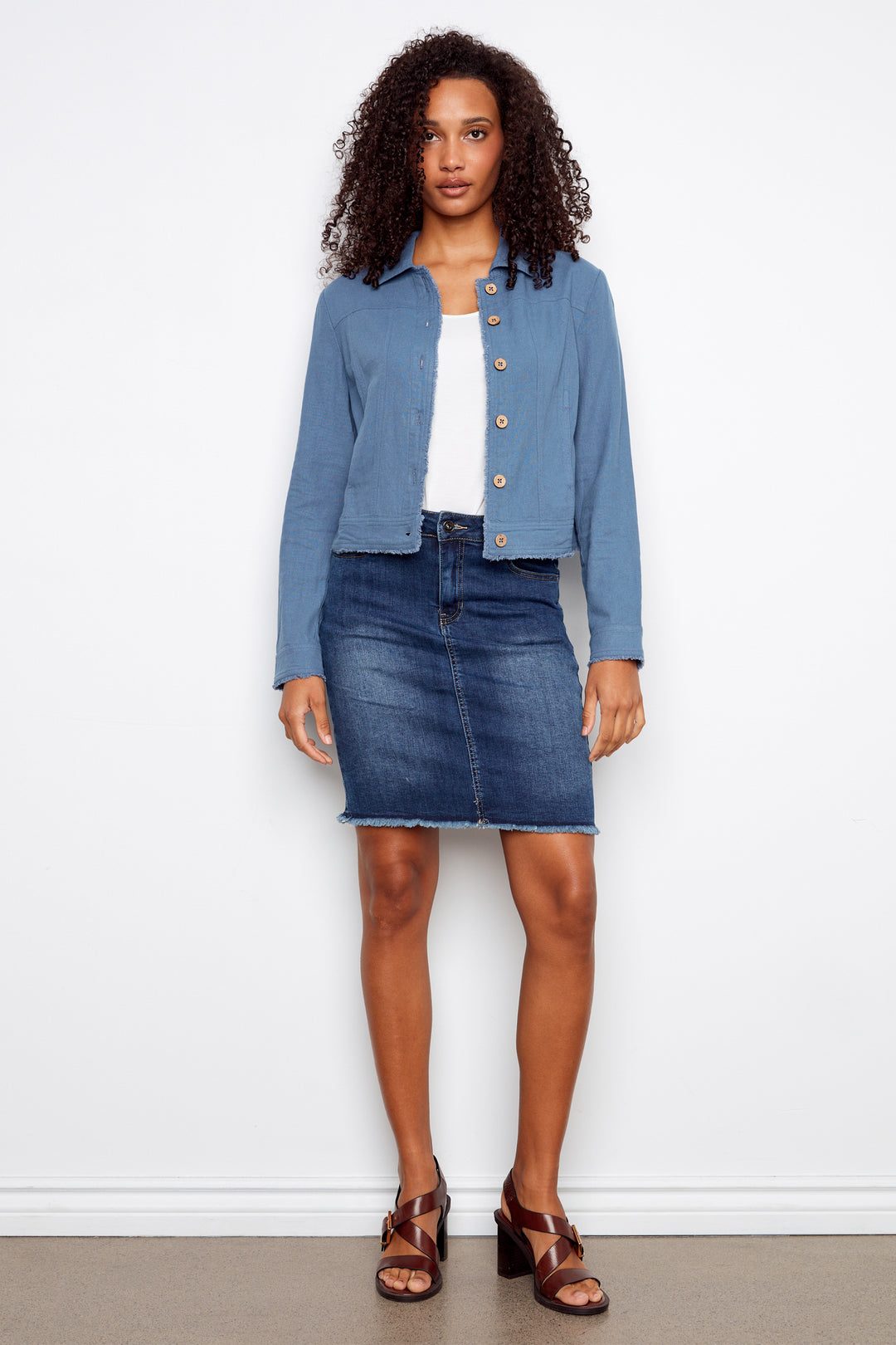 Woman wearing a blue denim jacket, white top, and skirt against a white background