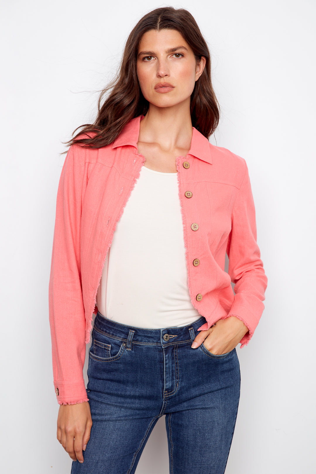 Woman wearing a pink jacket over a white top and blue jeans on a white background