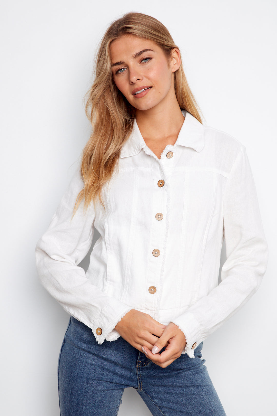 Woman wearing a white button-up shirt and blue jeans against a plain background