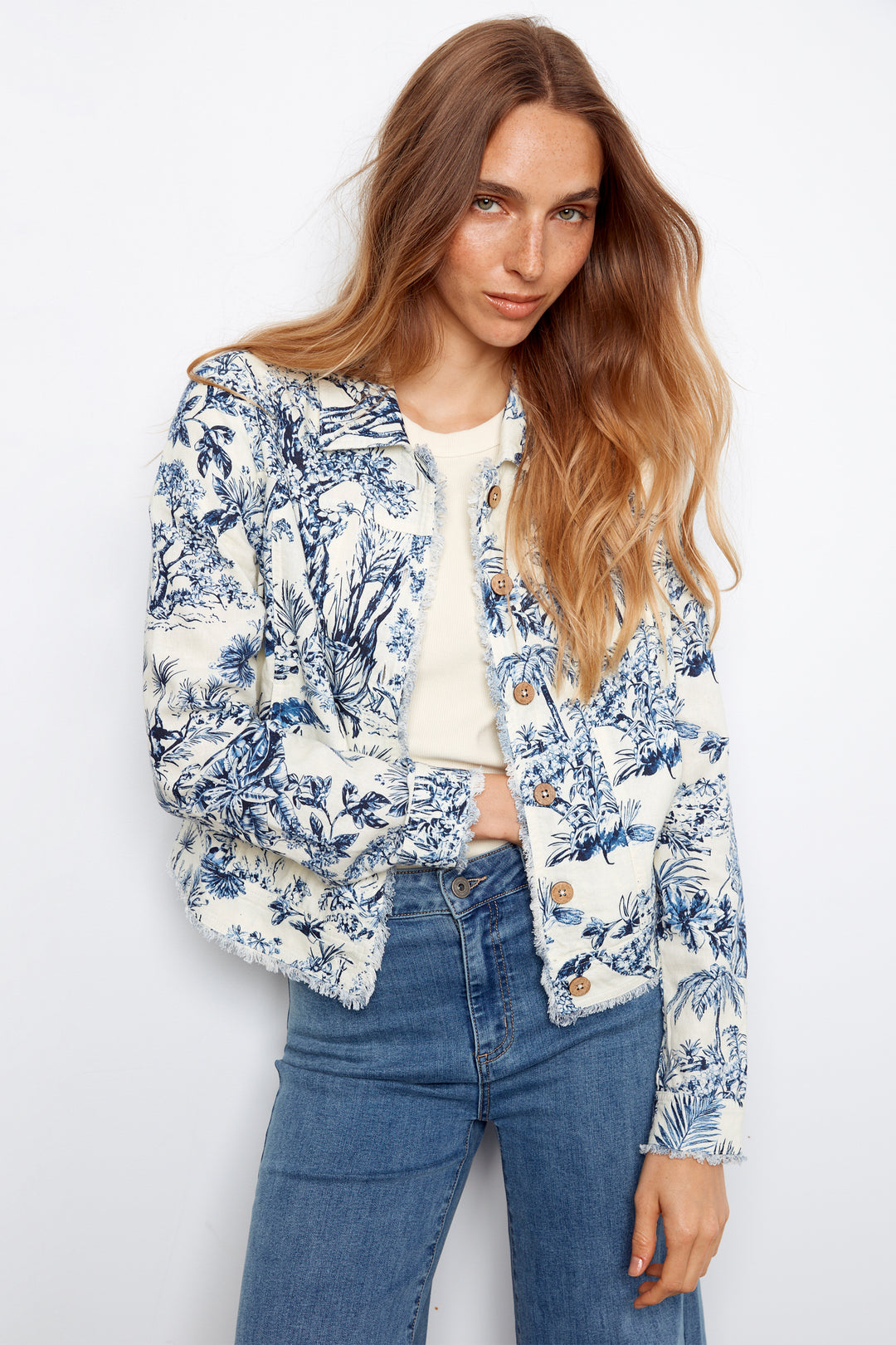 Woman wearing a floral jacket and blue jeans against a white background