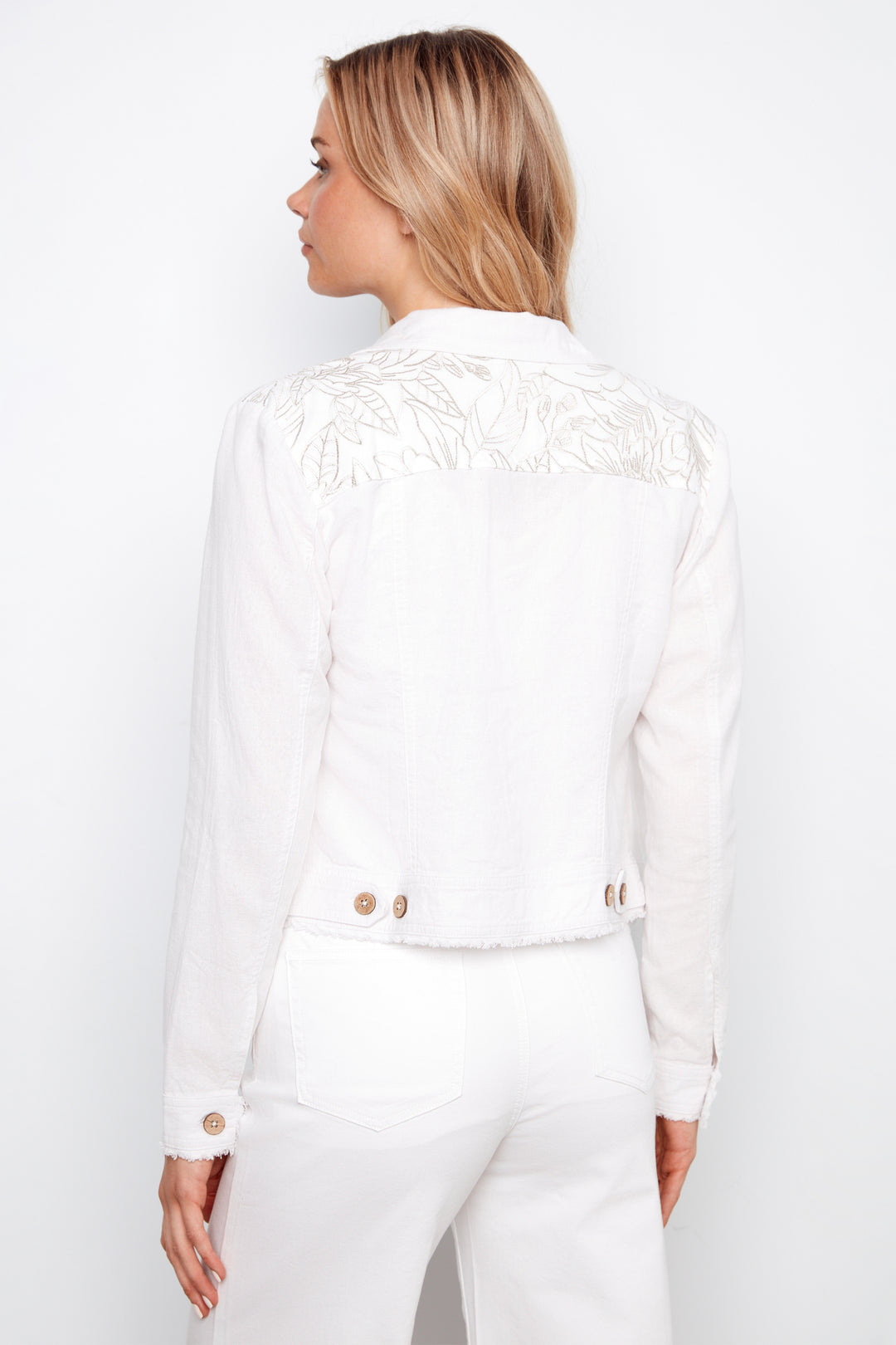 Woman wearing a white outfit with gold buttons on a plain background