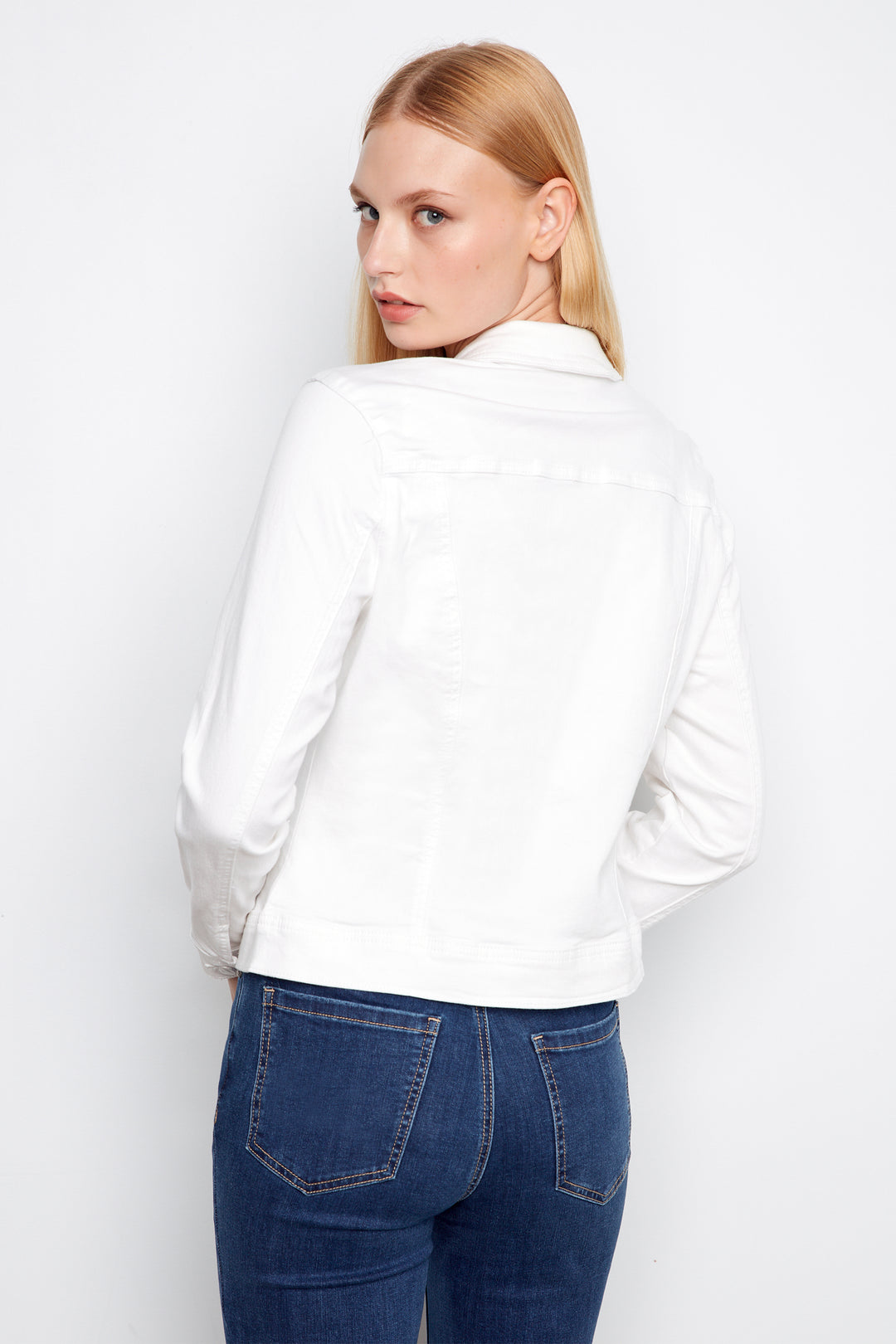 Woman wearing a white shirt and blue jeans against a plain background