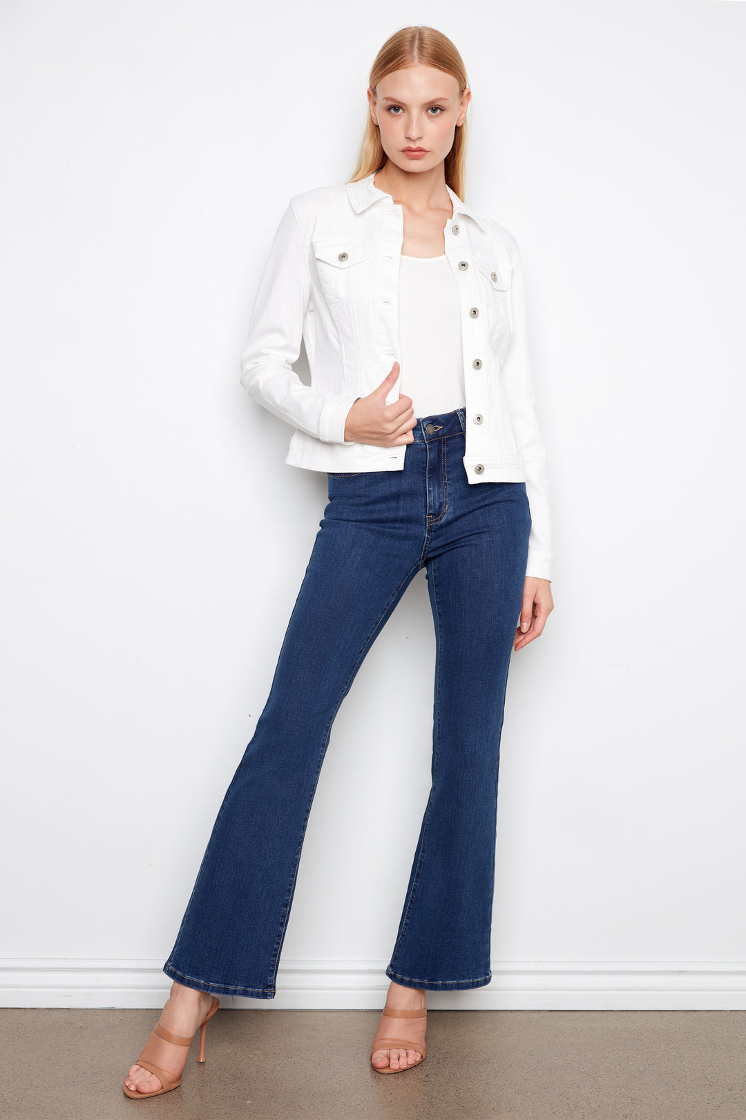 Woman wearing a white jacket and blue jeans against a white background