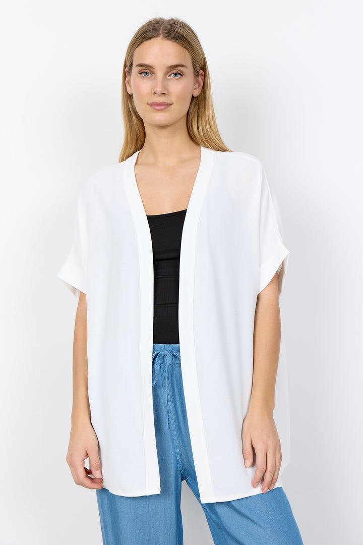 Woman wearing a white cardigan over a black top and blue pants on a white background