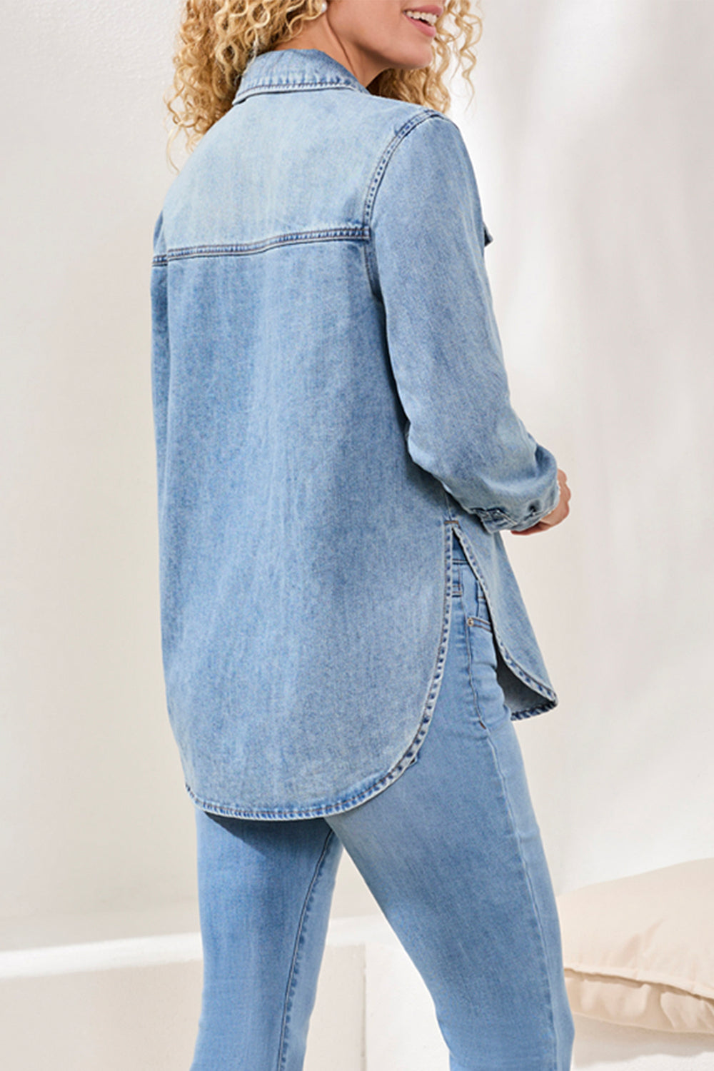 Person wearing a light blue denim shirt and jeans on a plain background