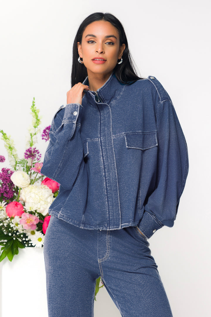 Woman wearing a blue denim sweater jacket and pants with flowers in the background