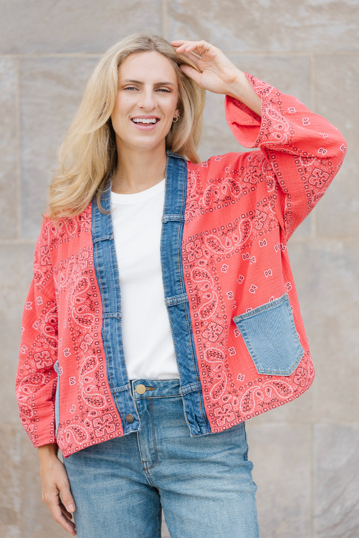 Woman wearing a red patterned open cardigan over a denim jacket with a neutral background