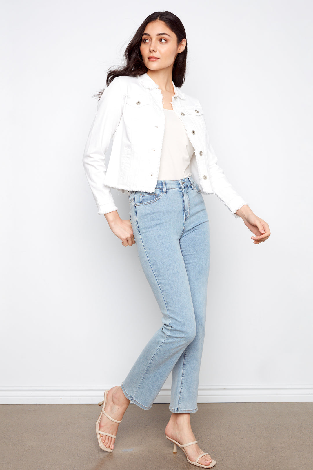 Woman wearing a white jacket, white shirt, and light blue jeans against a white background
