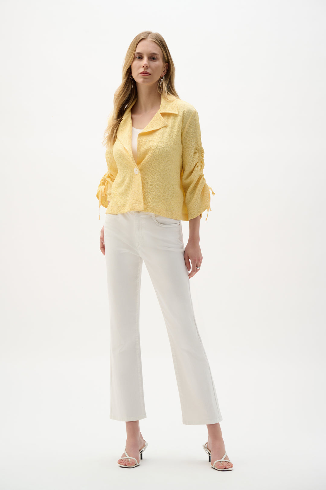 Woman wearing a yellow jacket and white pants on a white background