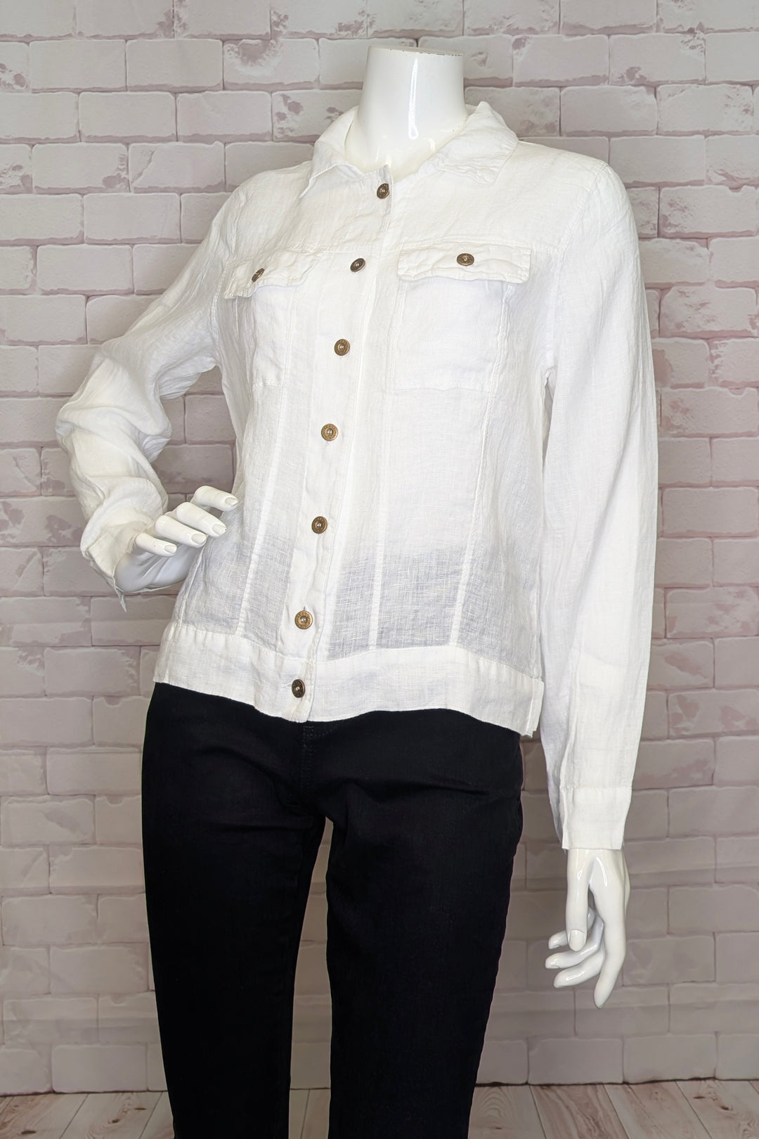 White sheer light linen jacket with button details on a mannequin against a white brick wall.
