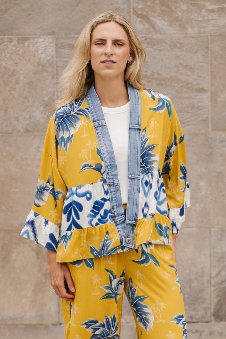 Woman wearing a yellow and blue floral cardigan against a beige wall.