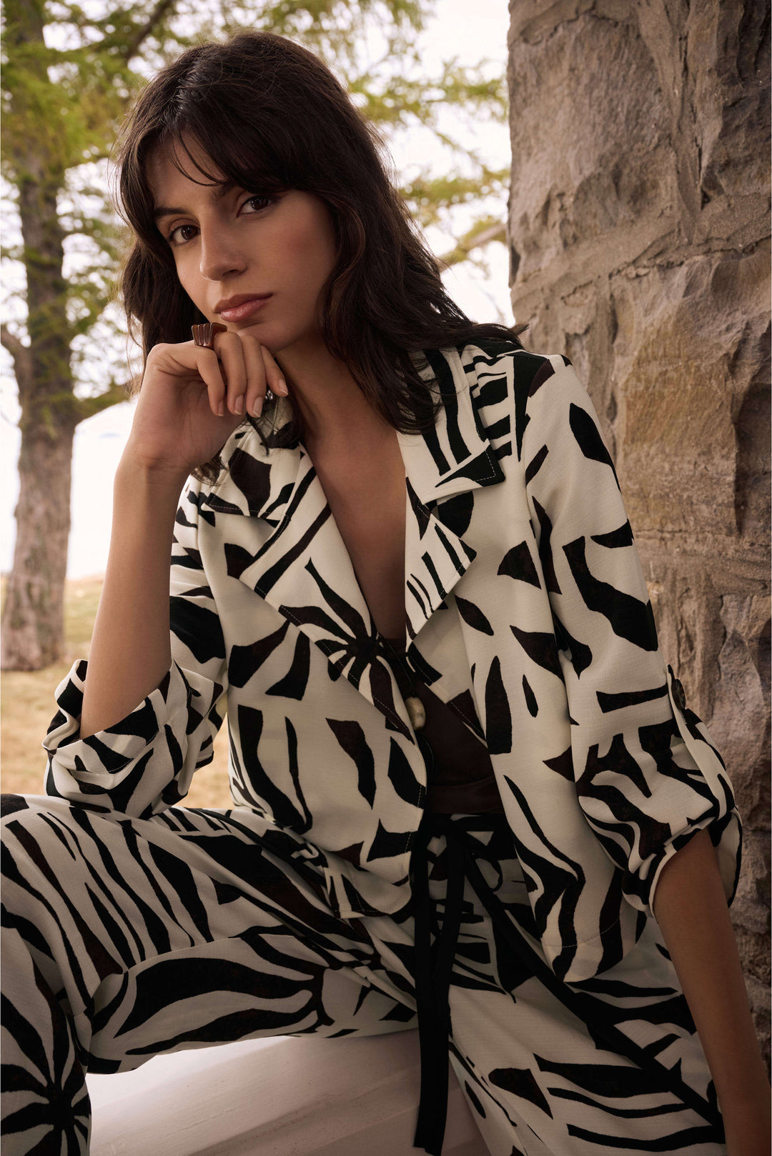 Woman wearing a black and white patterned outfit sitting against a stone wall.