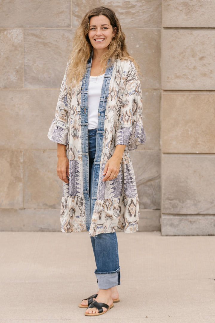Woman wearing a patterned kimono-style jacket standing against a stone wall.