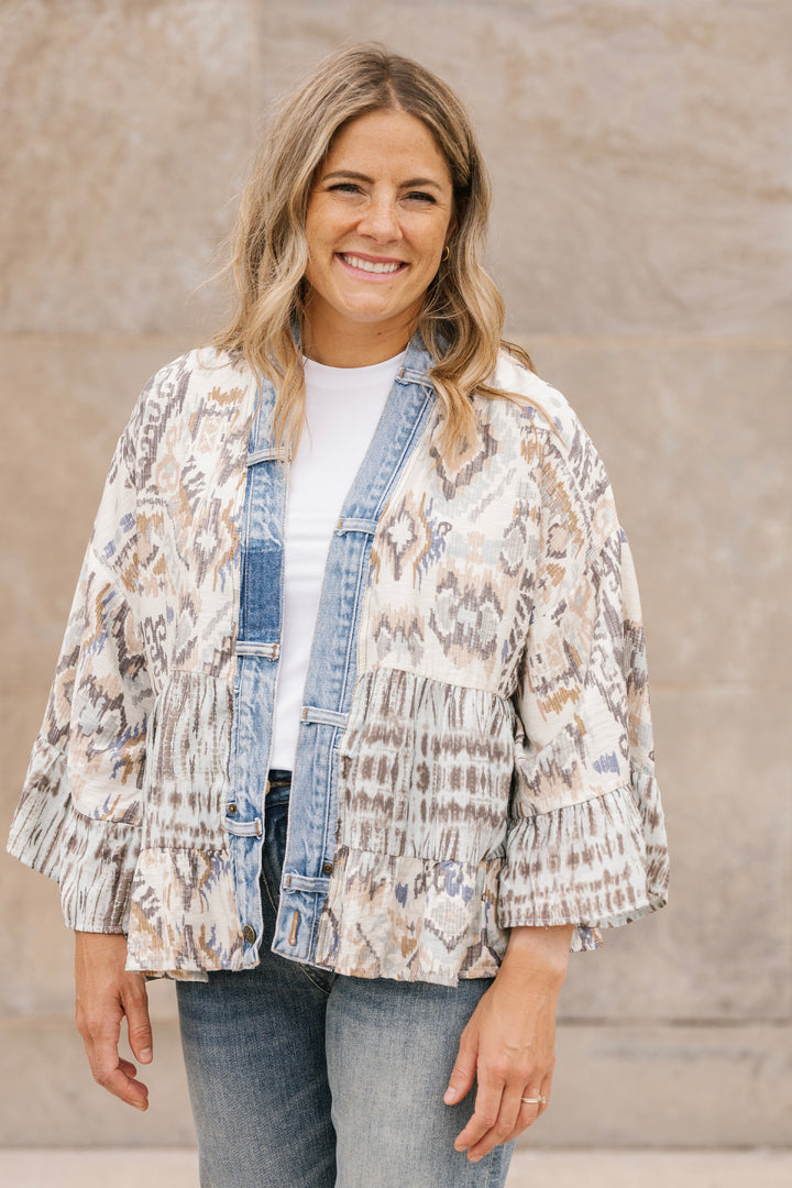 Woman wearing a patterned cardigan jacket over a denim shirt with a neutral background