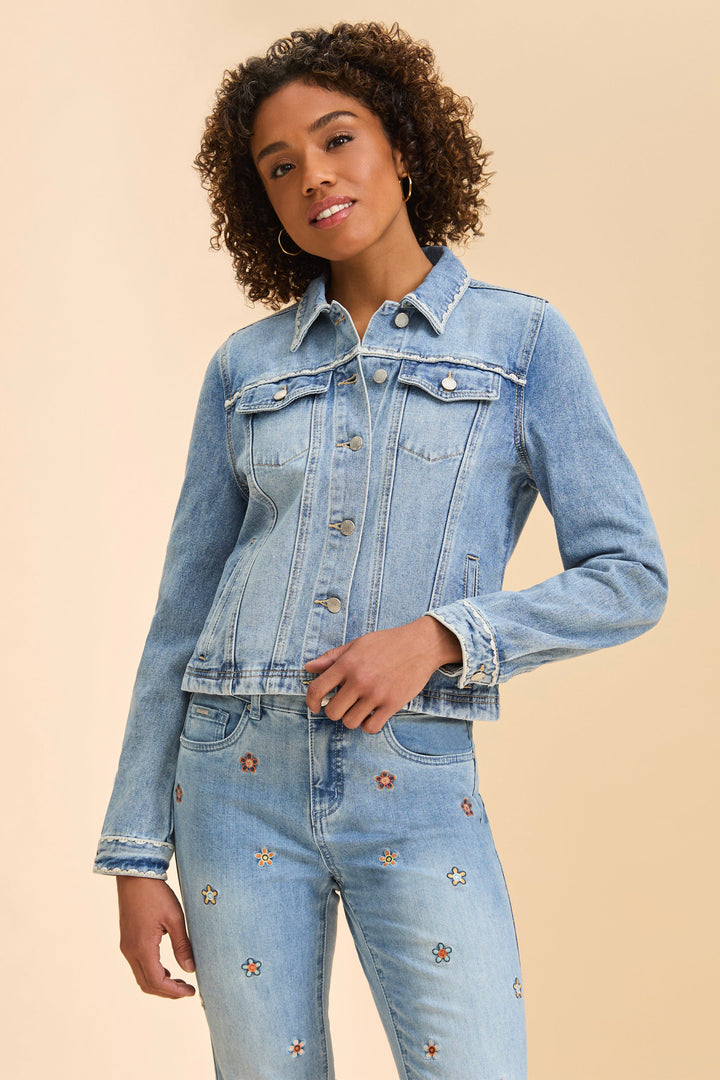 Woman wearing a light blue denim jacket with floral embroidery and jeans on a beige background