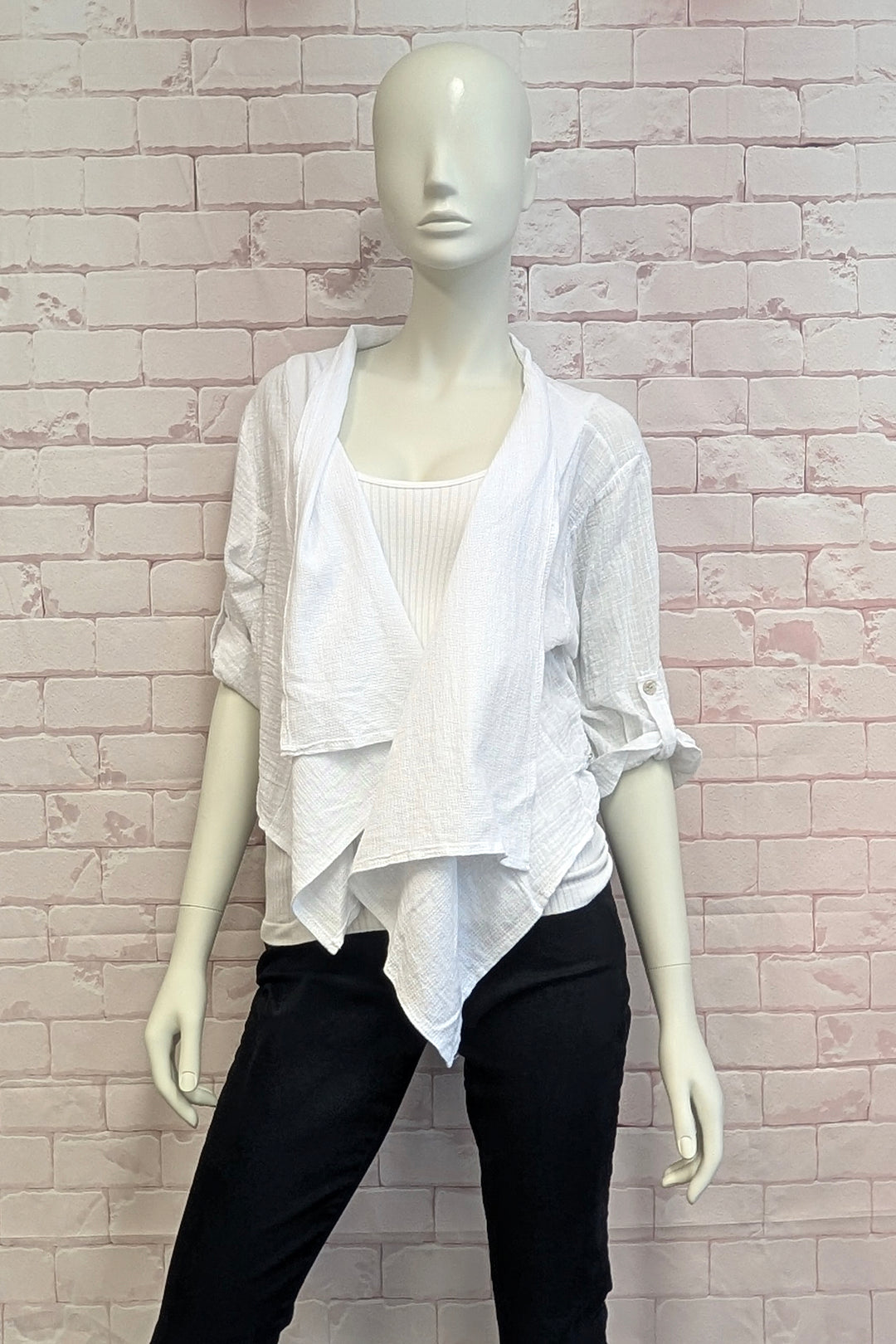 Mannequin wearing a white layered jacket and black pants against a light pink brick wall.
