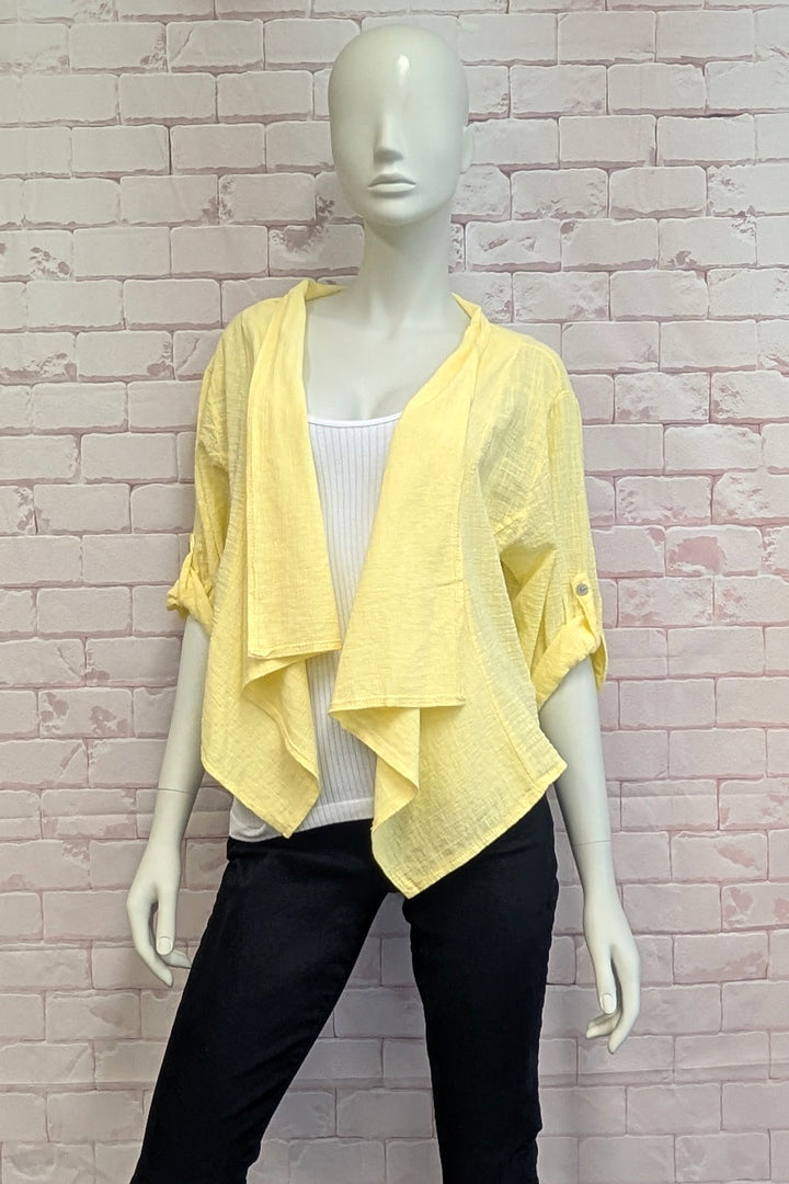 Mannequin wearing a yellow drape jacket over a white tank top and black pants against a light brick wall.
