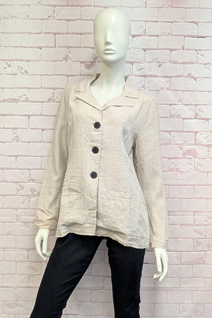 Mannequin wearing a beige button-up shirt with black buttons against a light brick wall.