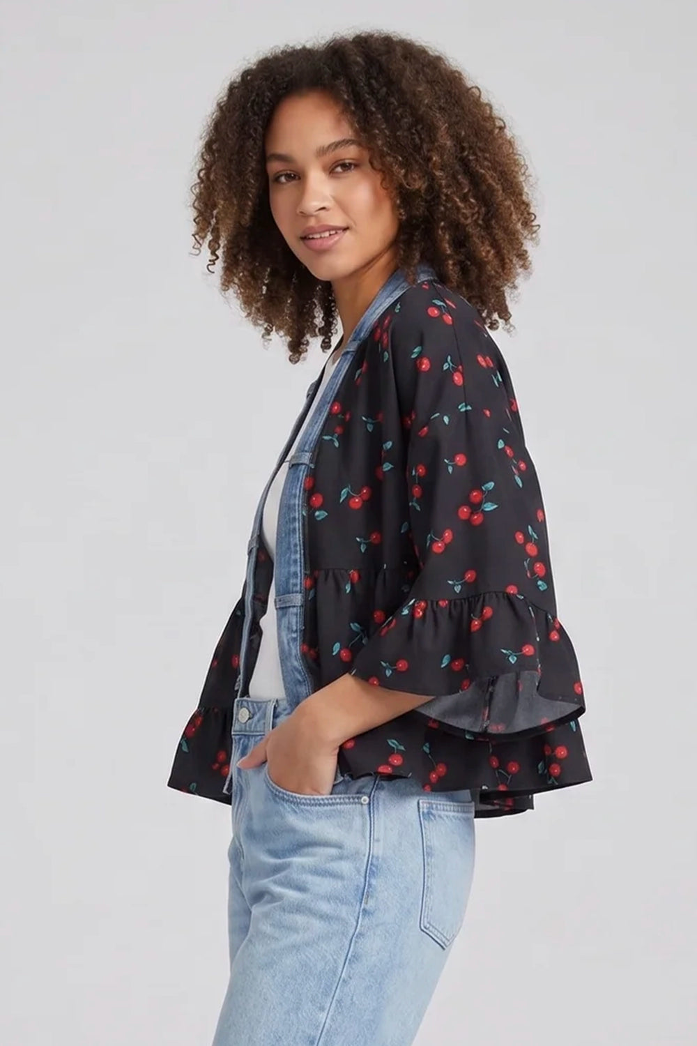 Woman wearing a black cherry print kimono jacket with light blue jeans on a plain background