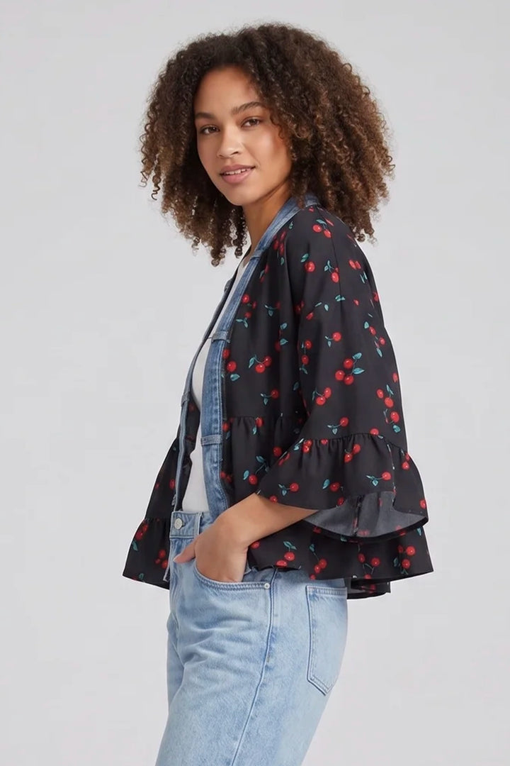 Woman wearing a black cherry print kimono jacket with light blue jeans on a plain background