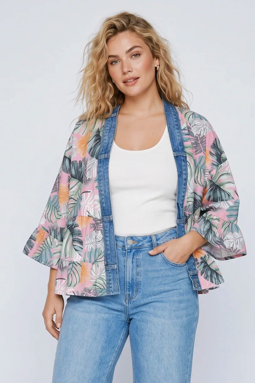 Woman wearing a floral kimono jacket over a white top and blue jeans on a light gray background