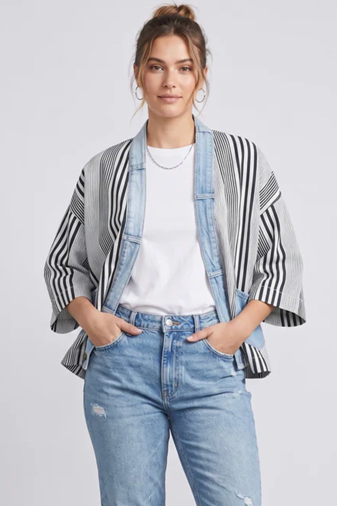 Woman wearing a striped kimono-style jacket over a white shirt and blue jeans on a light gray background