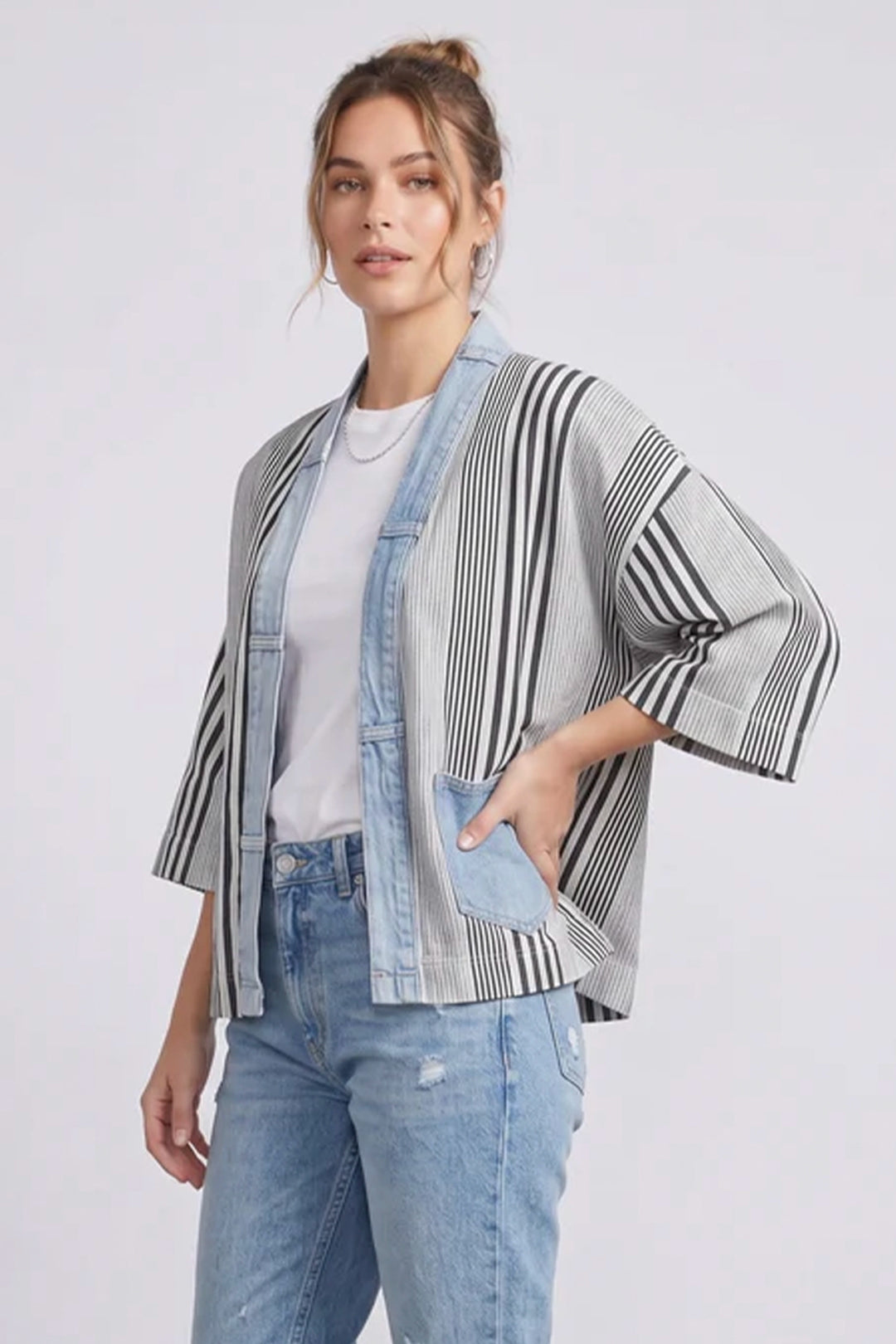 Woman wearing a striped kimono-style jacket and jeans on a white background