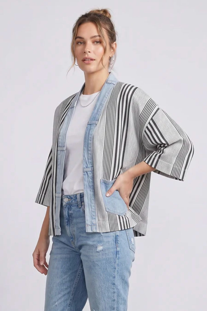 Woman wearing a striped kimono-style jacket and jeans on a white background