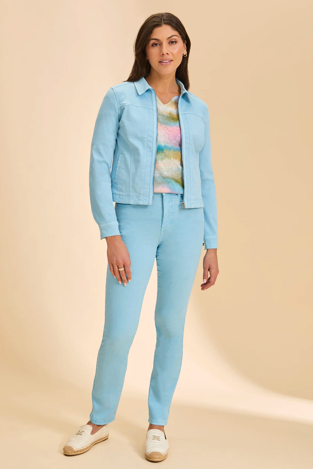 Woman wearing a light blue outfit with a jacket, shirt, and pants on a beige background