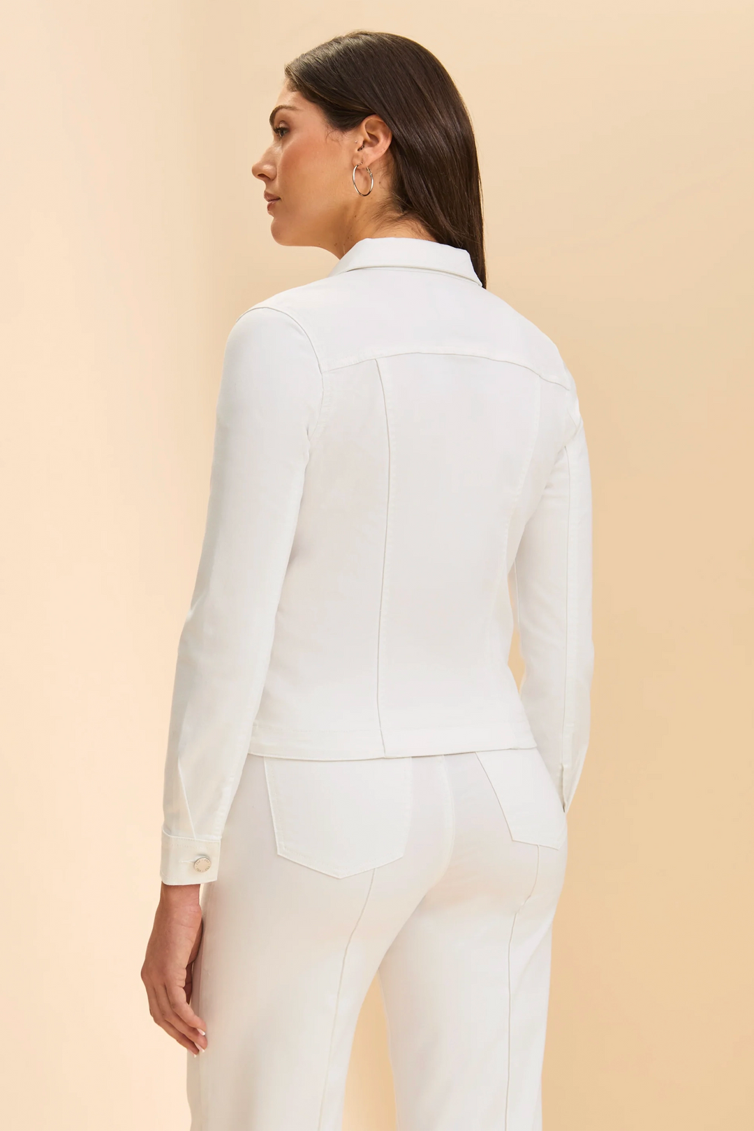 Woman wearing a white jacket and pants against a beige background